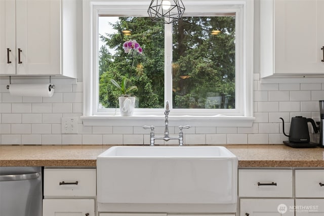 kitchen with stainless steel dishwasher, a sink, white cabinets, and backsplash