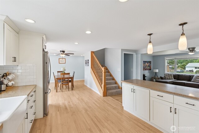 kitchen with a ceiling fan, light wood-type flooring, white cabinetry, open floor plan, and hanging light fixtures