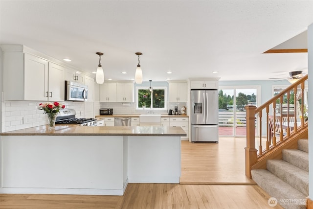 kitchen featuring stainless steel appliances, light wood finished floors, decorative backsplash, a sink, and a peninsula