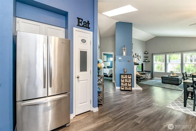 kitchen with vaulted ceiling, wood finished floors, baseboards, freestanding refrigerator, and white cabinetry