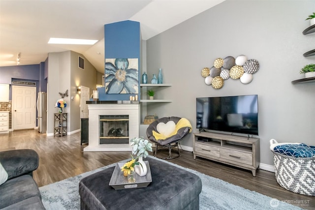 living room featuring visible vents, a brick fireplace, baseboards, wood finished floors, and vaulted ceiling