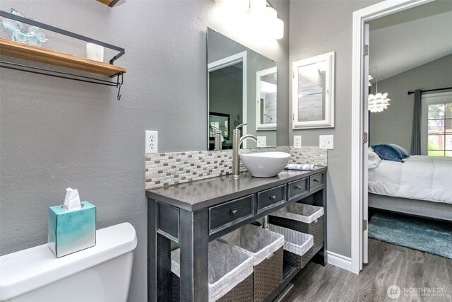 ensuite bathroom with ensuite bath, toilet, baseboards, wood finished floors, and tasteful backsplash
