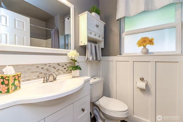 full bathroom featuring vanity, toilet, a shower with shower curtain, a wainscoted wall, and tasteful backsplash