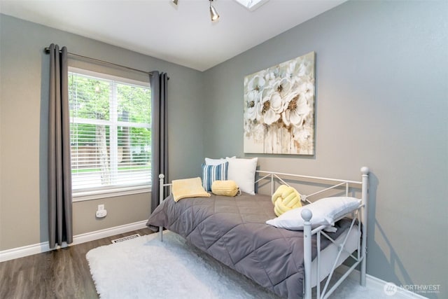 bedroom featuring baseboards, visible vents, multiple windows, and wood finished floors