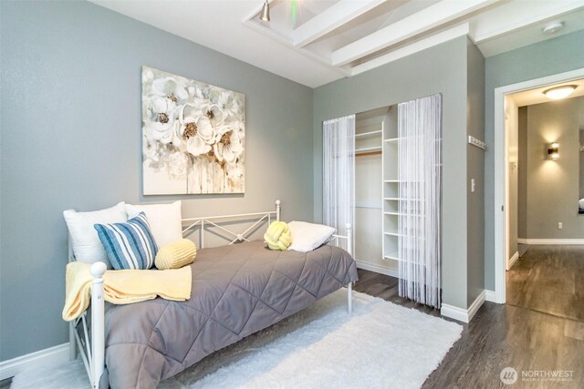 bedroom with baseboards, a closet, wood finished floors, and beam ceiling