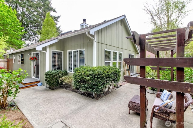 view of side of home with board and batten siding, a pergola, a chimney, and a patio