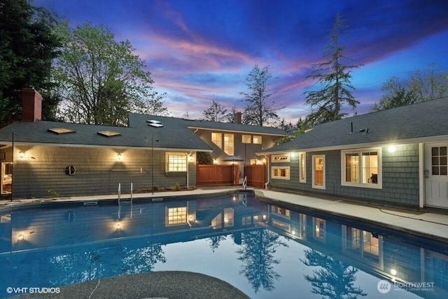 pool at dusk with an outdoor pool and fence