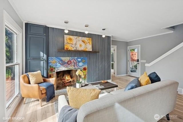 living area featuring crown molding, baseboards, light wood-type flooring, and a warm lit fireplace