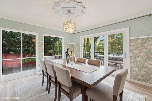 dining area with crown molding, wallpapered walls, and light wood-style flooring