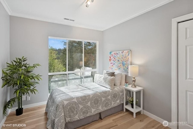 bedroom with baseboards, visible vents, ornamental molding, and wood finished floors