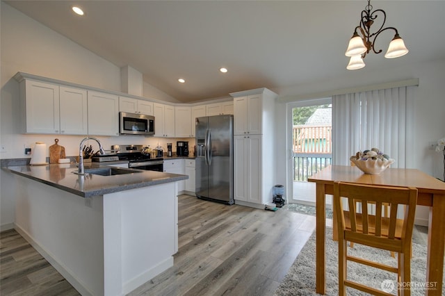kitchen with appliances with stainless steel finishes, a sink, white cabinets, a peninsula, and lofted ceiling
