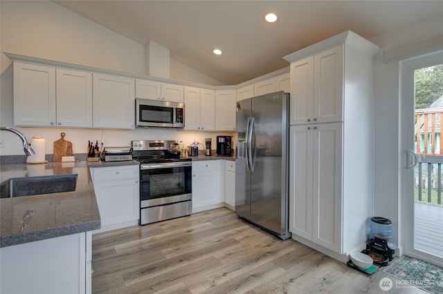 kitchen with light wood-type flooring, white cabinets, a sink, vaulted ceiling, and stainless steel appliances