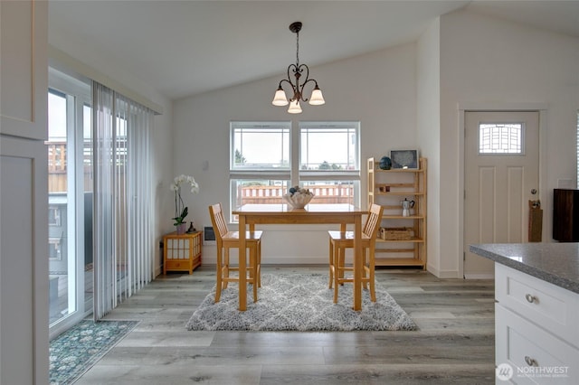 dining room featuring vaulted ceiling, a healthy amount of sunlight, an inviting chandelier, and light wood-type flooring