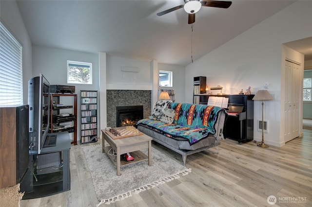 living room with ceiling fan, vaulted ceiling, wood finished floors, baseboards, and a glass covered fireplace