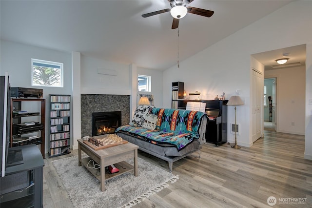 living area with a ceiling fan, baseboards, wood finished floors, vaulted ceiling, and a lit fireplace