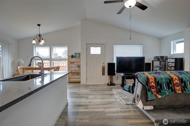 living area with ceiling fan with notable chandelier, light wood finished floors, and lofted ceiling