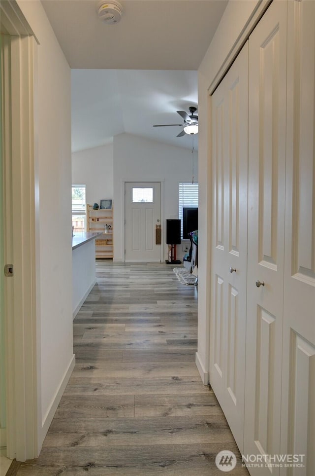 hall with baseboards, vaulted ceiling, and wood finished floors