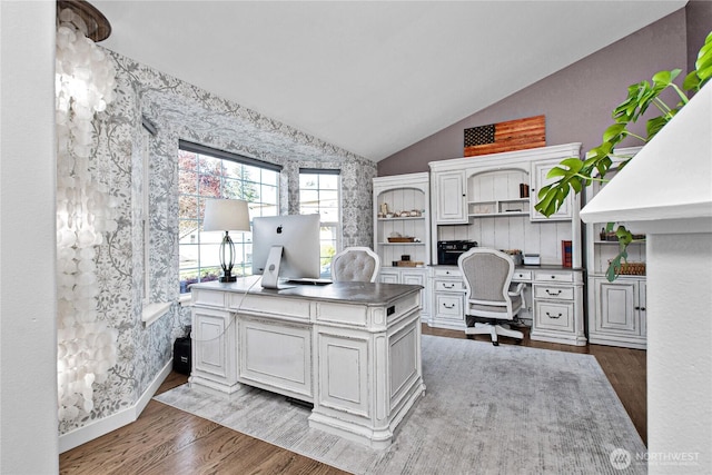 home office with lofted ceiling, wood finished floors, wallpapered walls, and built in study area