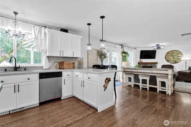 kitchen featuring a sink, open floor plan, dishwasher, dark wood-type flooring, and a peninsula