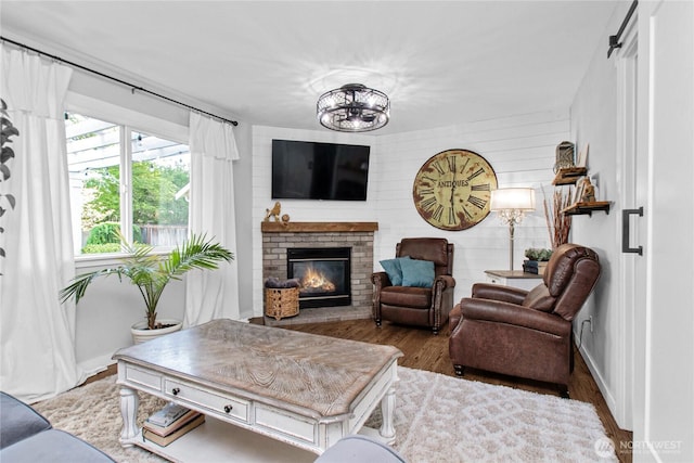 living room featuring a brick fireplace, a notable chandelier, wood finished floors, and baseboards
