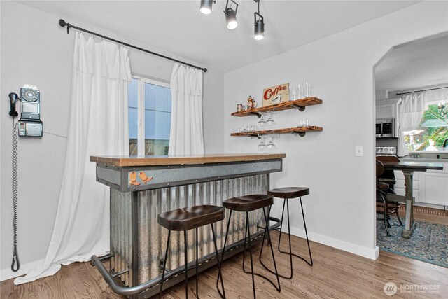 bar with stainless steel microwave, a bar, baseboards, arched walkways, and wood finished floors