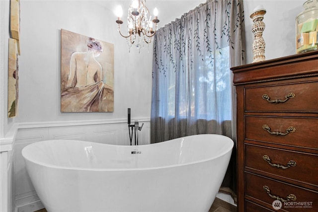 full bathroom featuring a wainscoted wall, a notable chandelier, a freestanding bath, and a decorative wall