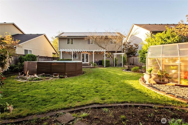 rear view of property with a pergola, an exterior structure, a yard, a fenced backyard, and roof mounted solar panels