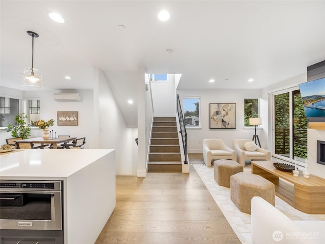 living area featuring light wood-style floors, a wall mounted air conditioner, recessed lighting, and stairs