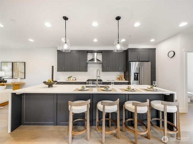 kitchen featuring high end fridge, wall chimney exhaust hood, a spacious island, backsplash, and light countertops