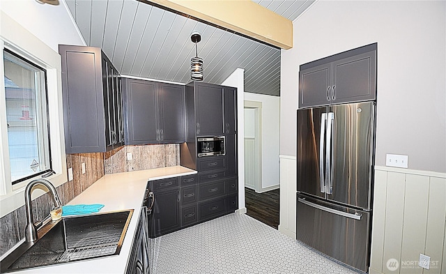 kitchen featuring decorative backsplash, stainless steel appliances, light countertops, a wainscoted wall, and a sink