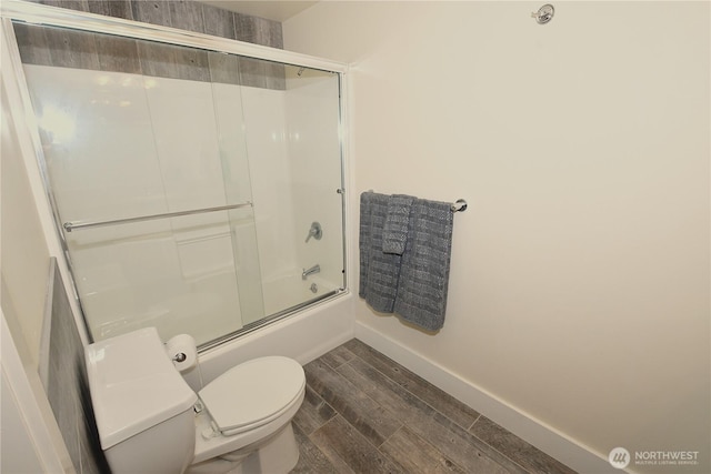 bathroom featuring baseboards, wood finished floors, bath / shower combo with glass door, and toilet