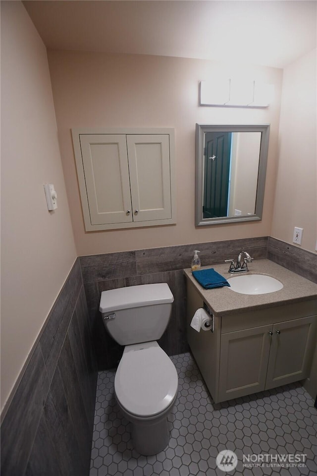 bathroom with toilet, a wainscoted wall, tile walls, and vanity