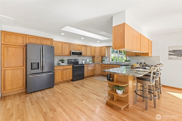 kitchen featuring stainless steel appliances, light wood-type flooring, tasteful backsplash, and a peninsula