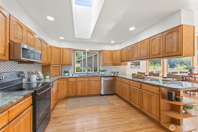 kitchen featuring a sink, light wood-style flooring, dark stone counters, stainless steel appliances, and a peninsula