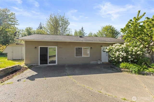 rear view of property featuring an outdoor structure, a patio, and a shed