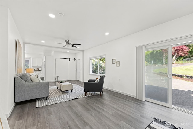 living area with ceiling fan, a barn door, wood finished floors, baseboards, and recessed lighting