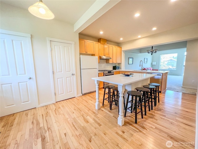 kitchen featuring light brown cabinetry, appliances with stainless steel finishes, light wood-type flooring, a peninsula, and under cabinet range hood