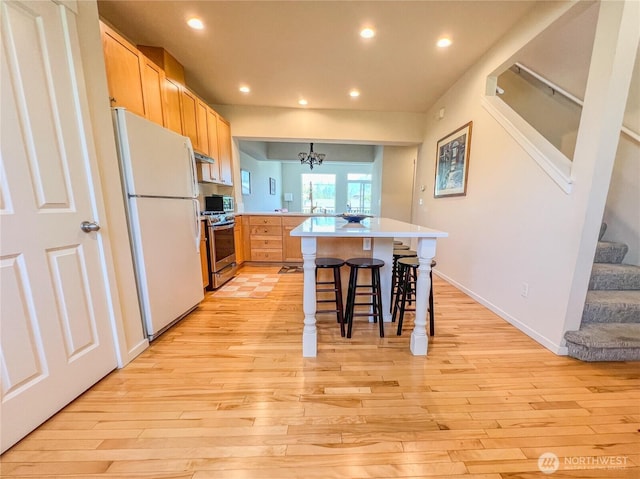 kitchen featuring stainless steel gas range, light wood finished floors, freestanding refrigerator, a peninsula, and recessed lighting