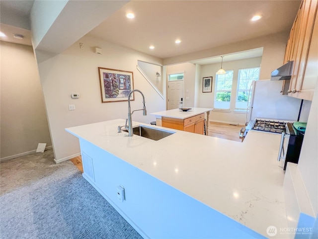 kitchen with wall chimney range hood, recessed lighting, a sink, and a center island