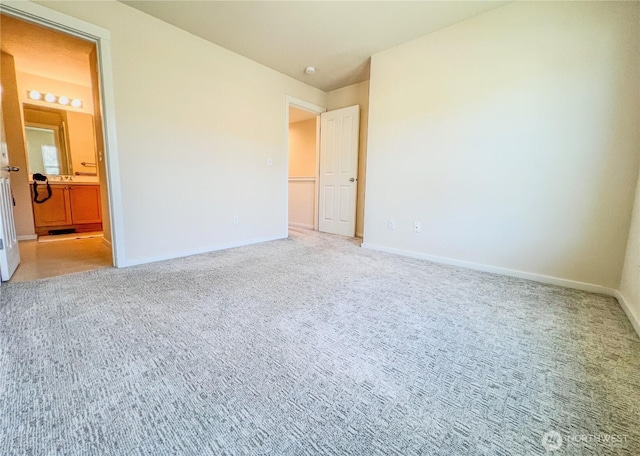 unfurnished bedroom featuring baseboards, light colored carpet, and ensuite bath