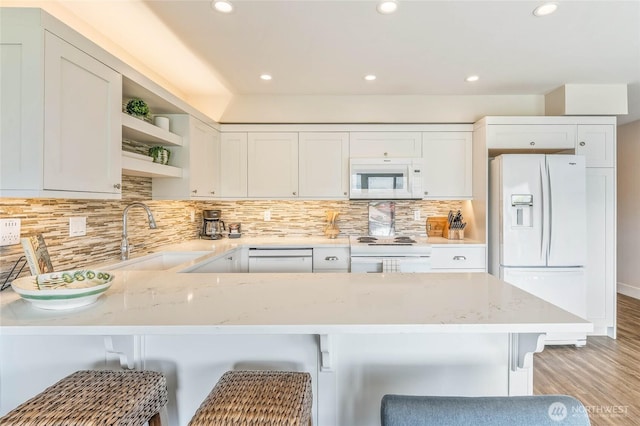 kitchen featuring open shelves, a sink, light stone countertops, white appliances, and a peninsula