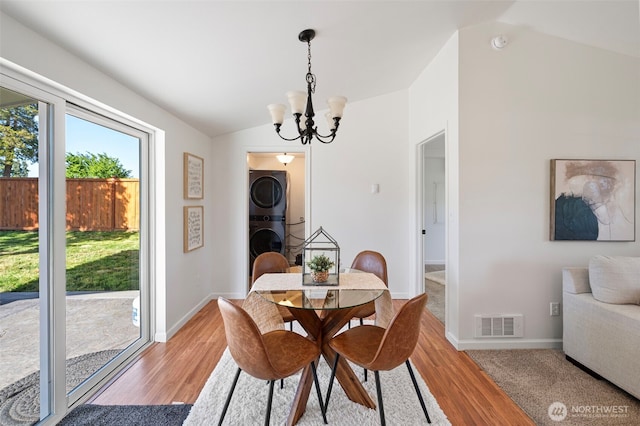 dining space featuring visible vents, stacked washing maching and dryer, a chandelier, light wood-style floors, and lofted ceiling