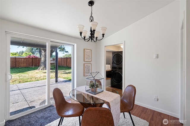 dining space featuring an inviting chandelier, baseboards, wood finished floors, and stacked washer / dryer