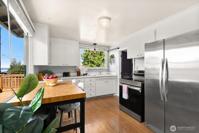 6357 37th Ave SW, Seattle, WA 98126 - kitchen with stainless steel appliances, light wood-style floors, white cabinetry, and decorative light fixtures