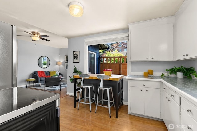6357 37th Ave SW, Seattle, WA 98126 - kitchen with light wood-style floors, white cabinets, a ceiling fan, and tile countertops