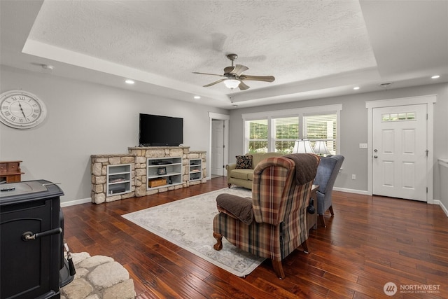 living area featuring a textured ceiling, ceiling fan, a tray ceiling, and dark wood finished floors