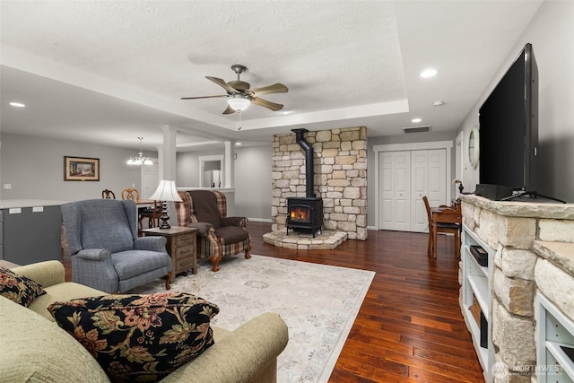 living area featuring dark wood-style floors, visible vents, a ceiling fan, a wood stove, and a tray ceiling