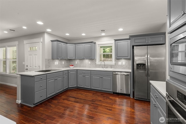 kitchen with appliances with stainless steel finishes, gray cabinetry, dark wood-style floors, and a peninsula