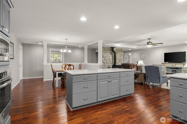 kitchen with a wood stove, light countertops, a kitchen island, open floor plan, and gray cabinets