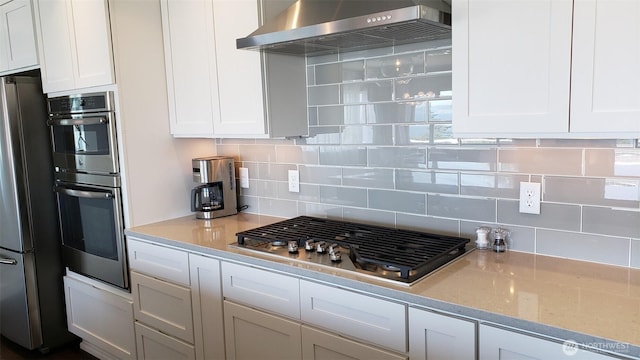 kitchen featuring wall chimney exhaust hood, appliances with stainless steel finishes, backsplash, and white cabinets